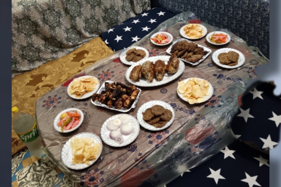 Традиционный египетский стол с разнообразными блюдами: жареная курица, фалафель, картофельные чипсы, хумус, маринованные овощи, салат и хлеб эйш. Еда подана на белых тарелках на низком столе с узорчатой скатертью. Семейная трапеза в египетском доме.